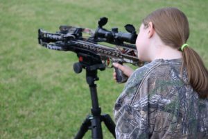 daughter - Crossbow Magazine Person in camouflage aiming a modern scoped rifle on a bipod in a grassy field.