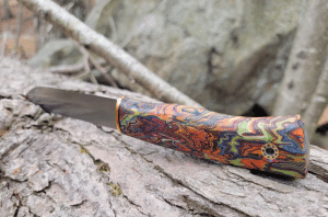 Colorful patterned knife with a dark blade resting on a rough log surface.