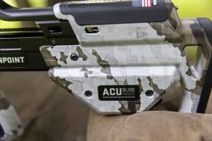 Close-up of a camouflage paintball marker with ACU SLIDE MAXX branding and safety text visible