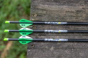 Arrows with bright green fletching lying on a weathered wooden surface, viewed side-on.