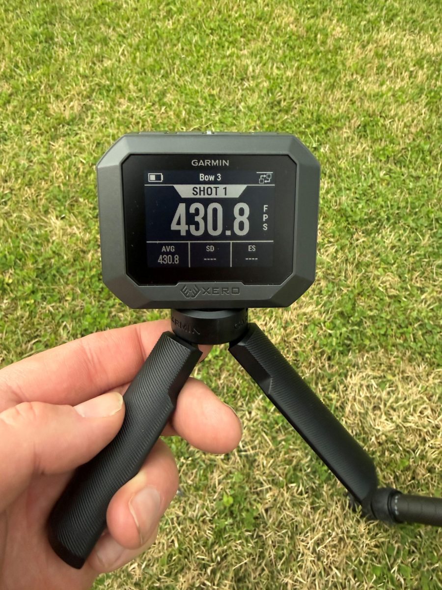 Close-up of a Garmin display unit mounted on a stand, held by a hand over green grass; screen shows SHOT 1 and 430.8.
