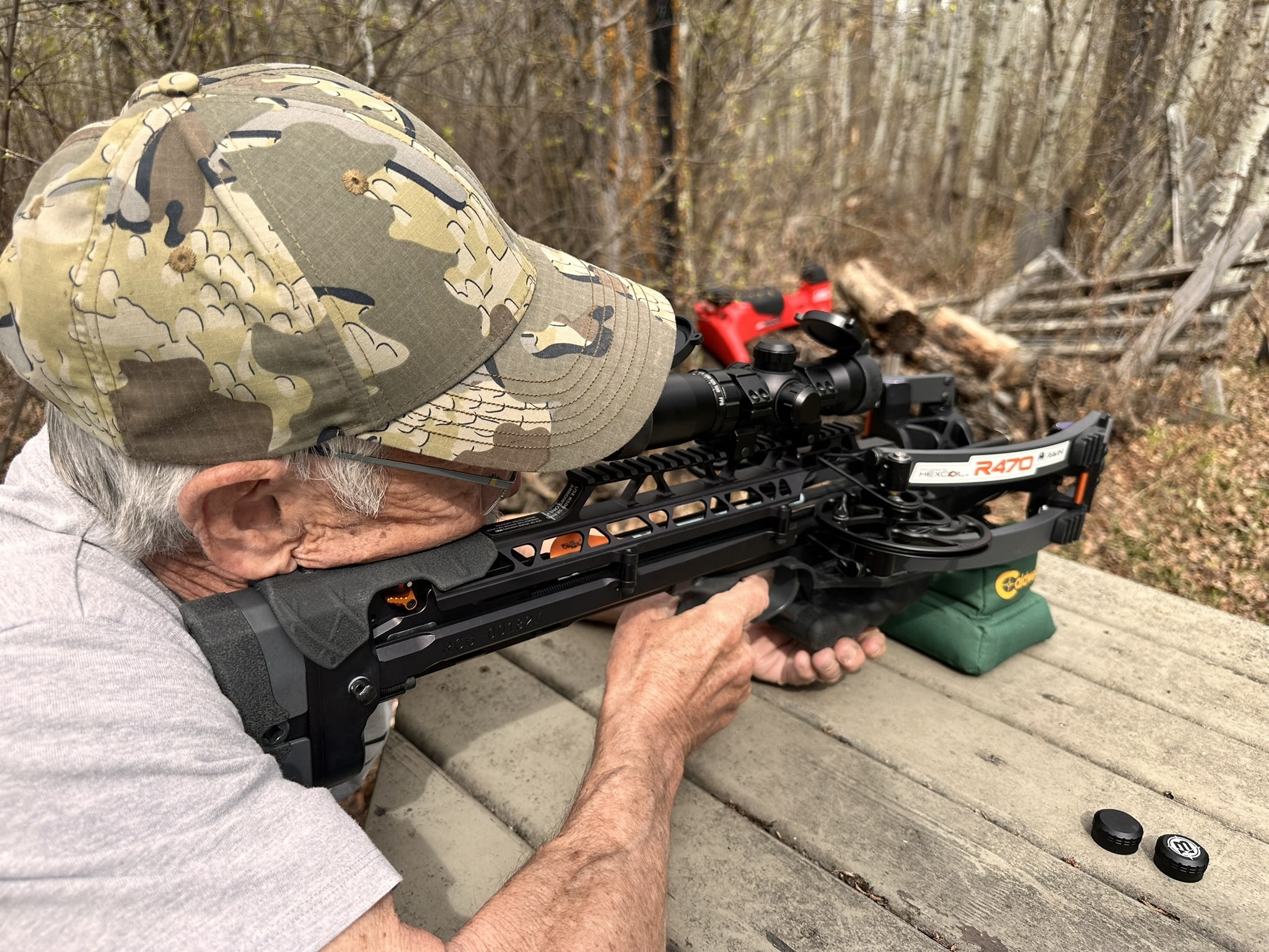 Person in a camouflage cap aiming a crossbow with a scope outdoors, focusing on the weapon's stock and sights.