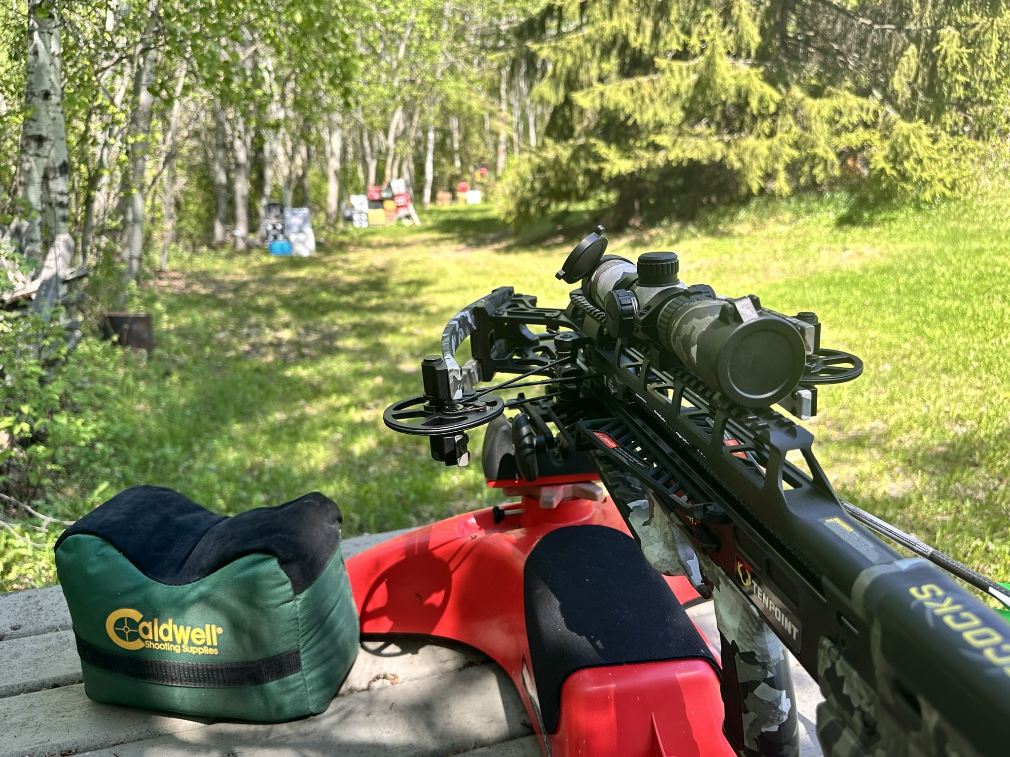 Crossbow with scope mounted on a red bench outdoors, Caldwell shooting bag in the foreground.