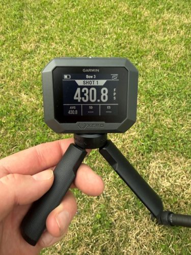Close-up of a Garmin display unit mounted on a stand, held by a hand over green grass; screen shows SHOT 1 and 430.8.