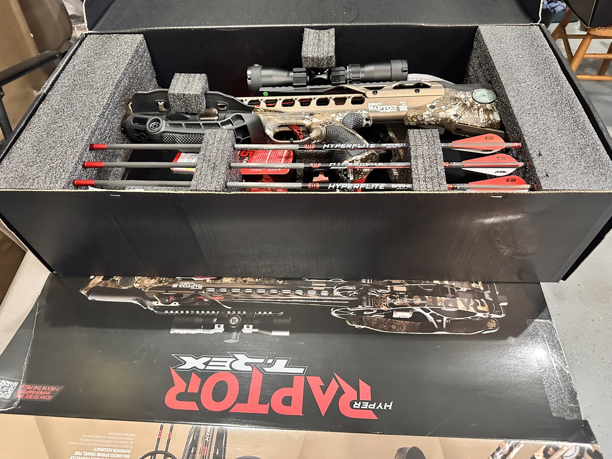 Camouflage Barnett TRex crossbow in a foam-lined case with a scope attached and four red-tipped arrows laid alongside it inside the case.